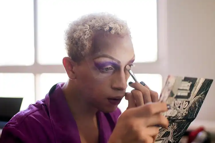 Person preparing makeup backstage at a pride event