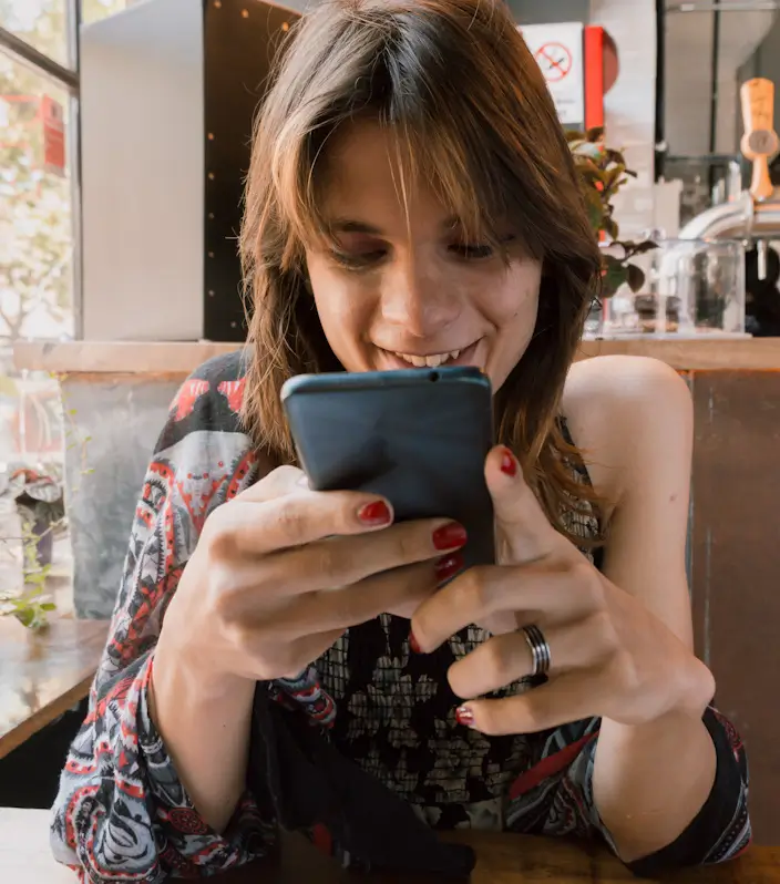 Persona sonriendo mientras lee mensajes en un teléfono en un entorno público casual