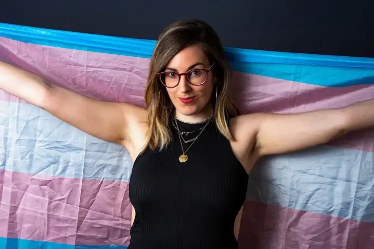 Smiling person holding a transgender flag outdoors